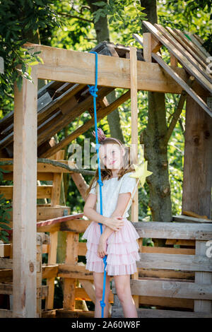 Ragazza vestita come una principessa con corona e scettro giocando in un albero di casa Foto Stock