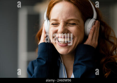 Ritratto di ridere redheaded imprenditrice ascolto di musica con cuffie bianche Foto Stock