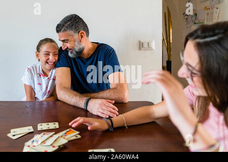 Padre Felice con due figlie giocando a carte sul tavolo di legno a casa Foto Stock