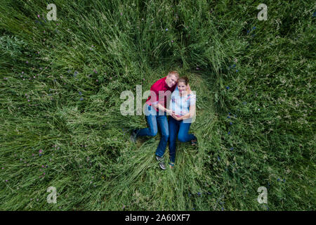 Donna incinta e uomo azienda baby pancia, giacente sul prato Foto Stock