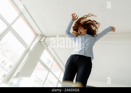 Redheaded donna in piedi sulla scrivania in un loft in movimento e urlando Foto Stock