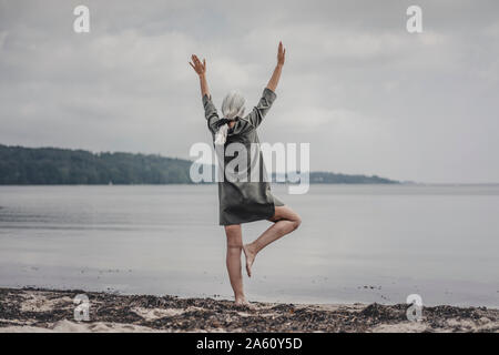 Senior donna che guarda al mare, in piedi su una gamba sola, vista posteriore Foto Stock