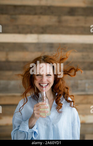 Ritratto di ridere redheaded donna con capelli di soffiatura di bere la limonata Foto Stock