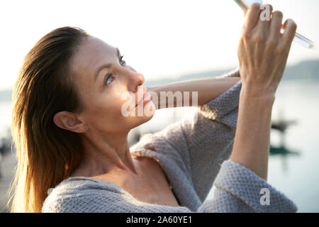 Donna matura cerca in mano specchio in un lago Foto Stock