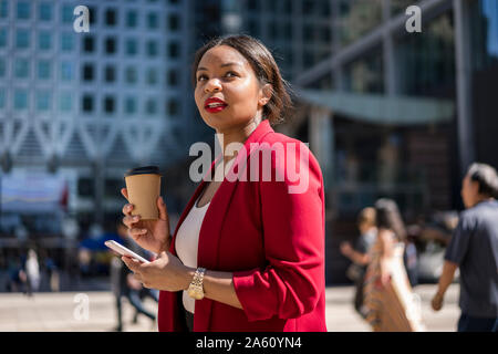 Ritratto di imprenditrice con caffè di andare e cellulare, London, Regno Unito Foto Stock