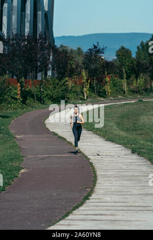 Giovane donna jogging in un parco lungo una di colore rosso e bianco modo Foto Stock