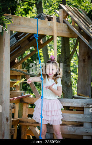 Ragazza vestita come una principessa con corona e scettro giocando in un albero di casa Foto Stock