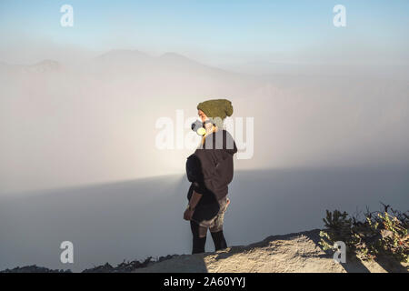 Giovane donna con maschera respiratore permanente al bordo del vulcano Ijen, Java, Indonesia Foto Stock