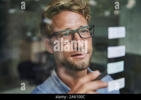 Casual giovane imprenditore con note adesive dietro il vetro di finestra di office Foto Stock