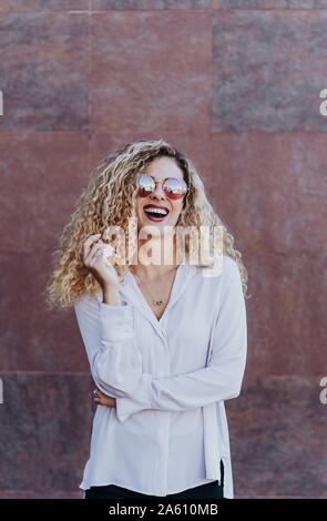 Ritratto di ridere giovane donna che indossa gli occhiali da sole Foto Stock