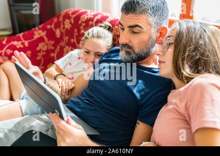 Padre di due figlie guardando tablet sul lettino a casa Foto Stock
