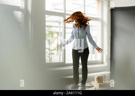 Redheaded donna in piedi sulla scrivania in un loft in movimento e urlando Foto Stock