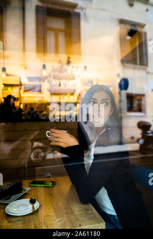 Giovane donna in un cafè dietro il vetro di finestra Foto Stock