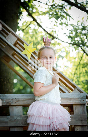 Ragazza vestita come una principessa con corona e scettro giocando in un albero di casa Foto Stock