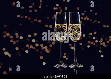 Due bicchieri di champagne su sfondo nero con golden bokeh di fondo. Natale e Anno Nuovo concetto. Foto Stock