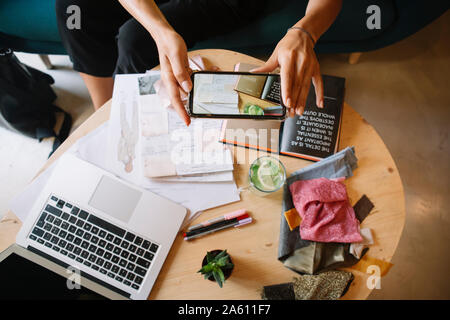 Close-up di fashion designer che lavora su una nuova collezione alla scrivania prendendo immagini dello smartphone Foto Stock