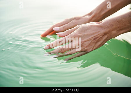 Close-up di donna di mani toccano acqua di lago Foto Stock