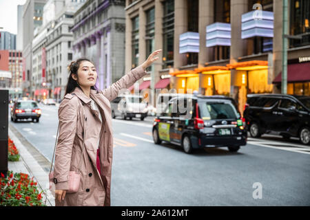 Giovane donna salutando un taxi a una strada a Ginza Tokyo, Giappone Foto Stock