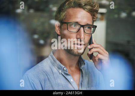 Casual giovane uomo d affari al telefono dietro il vetro di finestra di office Foto Stock