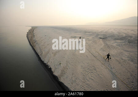 Tre uomini a sunrise rilasciando corde da un ormeggio in sabbia fine di un sandspit stagionali, fiume Brahmaputra, Assam, India, Asia Foto Stock