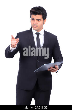 Bel giovane imprenditore puntando tenendo digitale compressa. Maschio è professionale dando la presentazione su mentre lo sfondo. Indossa il vestito. Foto Stock