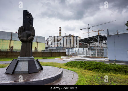 Monumento a la catastrofe di Cernobyl liquidatori con il quarto reattore sullo sfondo Foto Stock