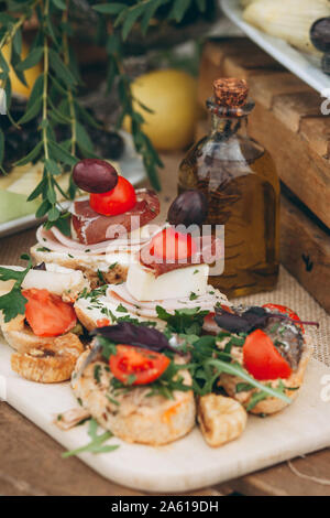 Close up dei panini con il formaggio e la carne e gli altri prodotti alimentari e una bottiglia di olio d'oliva sul tavolo. Foto Stock