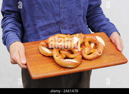 Uomo in lino blu shirt portante una tavola di legno con pretzel bavarese Foto Stock