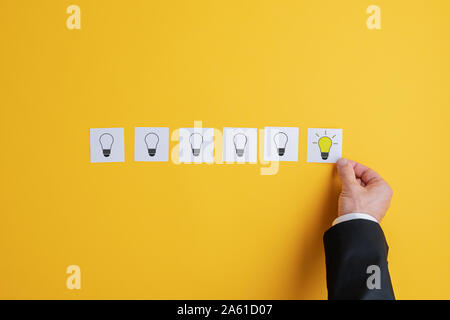 La mano di un uomo d affari con immissione sei post documenti it con lampadina di luce su di essi in una fila con l'ultima lampadina incandescente. Su sfondo giallo. Foto Stock