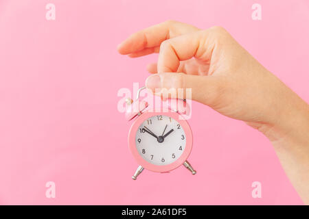 Design semplicemente donna femmina mano azienda squillo campana doppia sveglia isolato sul pastello rosa colorato sfondo alla moda. Resto ore di tempo di vita Buongiorno notte svegliarsi svegli concetto. Spazio di copia Foto Stock