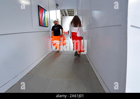 Londra, Inghilterra, Regno Unito. Giovane donna in bianco superiore e mantello rosso camminare sotto i ponteggi nel filamento Foto Stock
