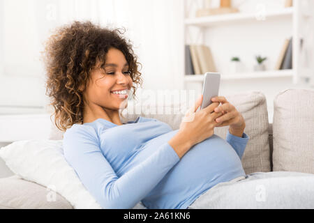 Felice donna incinta navigando in rete sullo smartphone Foto Stock