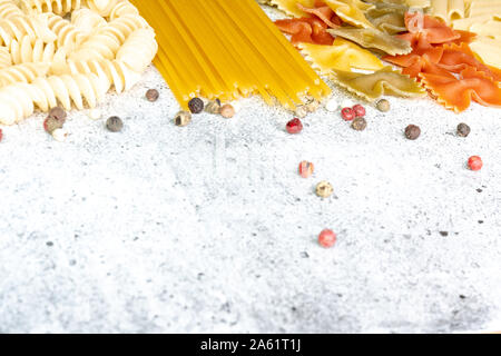 Tipi di pasta cruda. Pasta penne, fusilli, farfalle, non cotti gli spaghetti su un calcestruzzo leggero sottofondo. Laici piana, copia dello spazio. Foto Stock