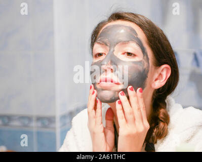 La ragazza si prende cura per la pelle grassa. Procedure cosmetiche. La cura della pelle. Giovane donna con un nero maschera di fango sul suo viso. pulizia pori. Procedure cosmetiche. Foto Stock