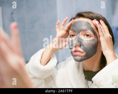 La ragazza si prende cura per la pelle grassa. Procedure cosmetiche. La cura della pelle. Giovane donna con un nero maschera di fango sul suo viso. pulizia pori. Procedure cosmetiche. Foto Stock