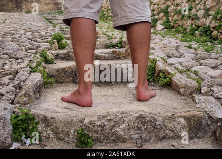 Un uomo con i piedi nudi gambe conciate passeggiate su una scala di pietra, close-up Foto Stock