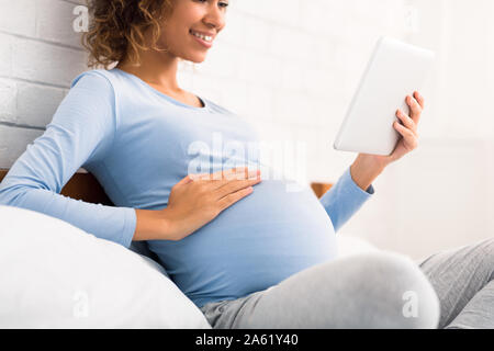 Giovane donna incinta toccando il suo ventre, utilizzando tablet Foto Stock