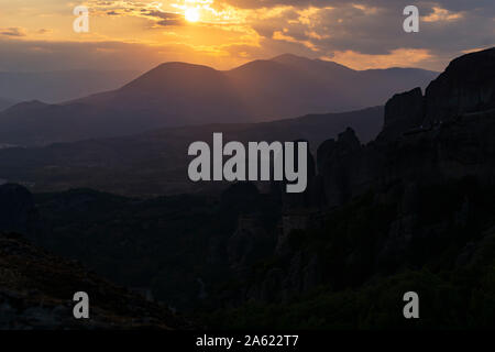 Sole che tramonta dietro le nuvole drammatico e oltre la sagoma scura delle montagne di Meteora in Grecia. Foto Stock