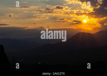 Sole che tramonta dietro le nuvole drammatico e oltre la sagoma scura delle montagne di Meteora in Grecia. Foto Stock