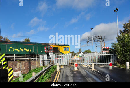 Freightliner classe 66 traina un nolo per ora chiuso passaggio a livello Ely (cattedrale west tower a distanza), Cambridgeshire, England, Regno Unito Foto Stock