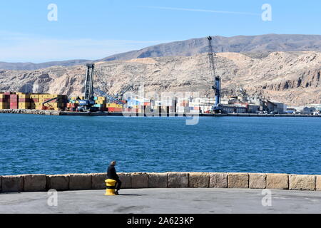 Uomo seduto su un bollard guardando attraverso il porto di Almeria, Almeria, Spagna Foto Stock