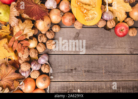 In autunno la disposizione dei raccolti stagionali con foglie colorate. Vista dall'alto di verdura e frutta come mele, zucca, noci, cipolle. Copia dello spazio. Foto Stock