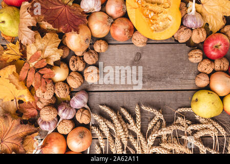 In autunno la disposizione dei raccolti stagionali con foglie colorate. Vista dall'alto di verdura e frutta come mele, zucca, noci, cipolle. Copia dello spazio. Foto Stock