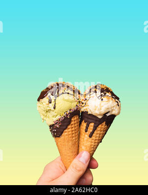 Il gelato in coni tenuto nel palmo della tua mano. I wafer e il dessert con cioccolato topping e spruzzi di colore su un background color pastello. Un dolce Foto Stock