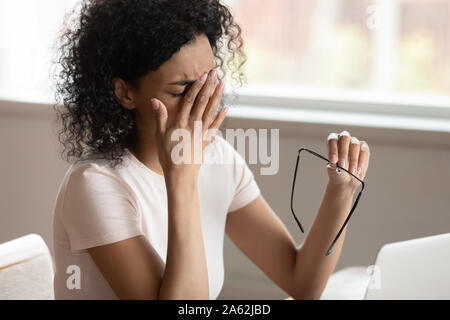 Stanco African American millennnial donna la caduta di occhiali, strofinarsi gli occhi. Foto Stock