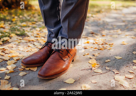 Imprenditore indossando scarpe in autunno park. In pelle marrone calzature classiche. Govern vestito. Close up di gambe Foto Stock