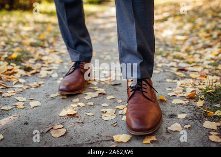 Imprenditore indossando scarpe in autunno park. In pelle marrone calzature classiche. Govern vestito. Close up di gambe Foto Stock