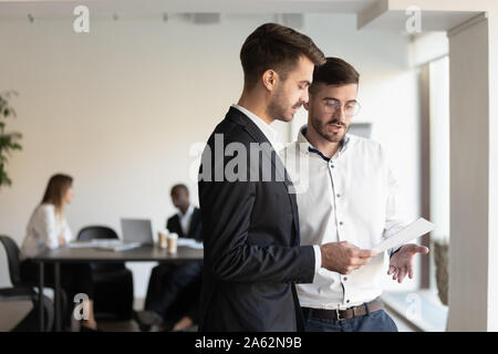 Grave dirigenti maschi discutere la relazione della documentazione in piedi in ufficio Foto Stock