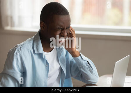 Infelice stanco african american guy affetti da forti improvvisi mal di testa. Foto Stock