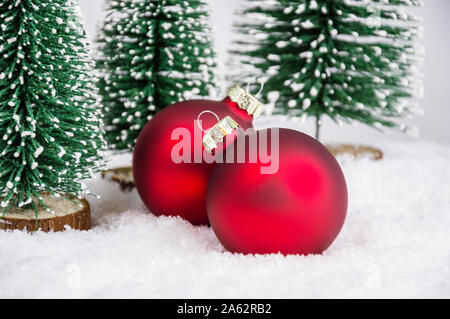 Close-up di due rosso palle di Natale sulla neve tra piccolo giocattolo di abeti. Decorazione di natale in tema foresta giocattolo. Merry Christmas greeting card e hol Foto Stock